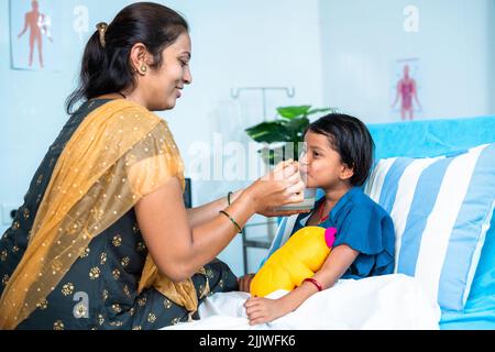 Mother feeding porridge to ill kid while admitted at hospital ward - concept of parental caring, medical treatment and health care. Stock Photo