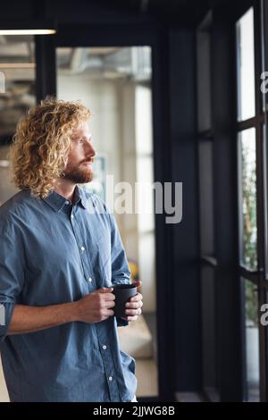 Thoughtful caucasian young businessman having coffee while looking through window Stock Photo
