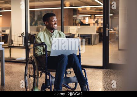 Smiling african american businessman with disability using laptop in wheelchair Stock Photo