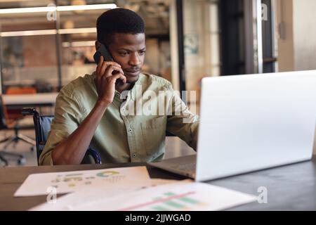 Determined african american businessman with disability talking on phone and using laptop Stock Photo