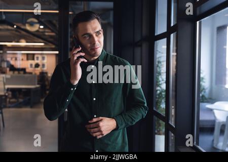Caucasian young businessman talking through smart phone by window at creative office Stock Photo
