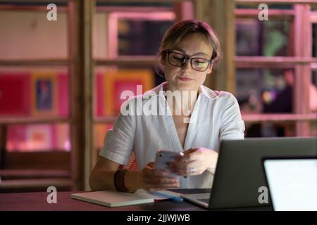 Female employee using mobile device at workplace, young woman freelancer distracted by smartphone Stock Photo