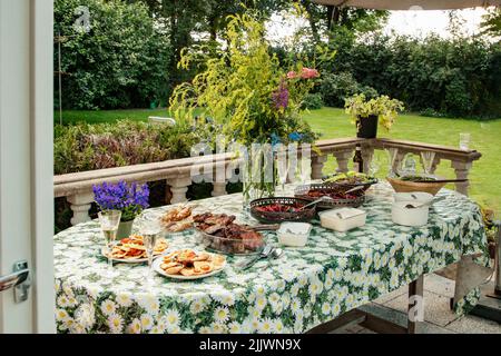 Festive buffet table with vegetarian dishes at a party in the garden. Outdoor ceremony with catering. Buffet with delicacies, decorated with wildflowe Stock Photo