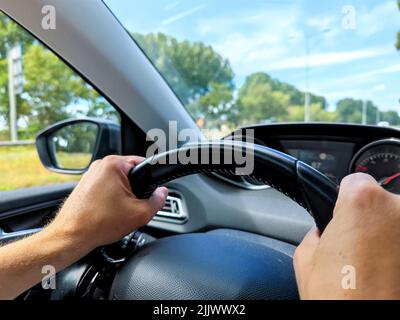 White men hands control a car steering wheel while driving on the road. There are no recognizable persons or trademarks in the shot. Stock Photo