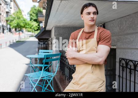 Young salesman in apron looking away on terrace of sweet shop Stock Photo