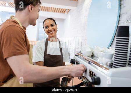 Smiling african american seller looking at barista making coffee in confectionery Stock Photo