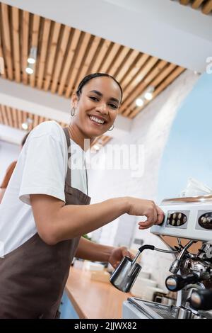 Low angle view of smiling african american barista making coffee and looking at camera in confectionery Stock Photo