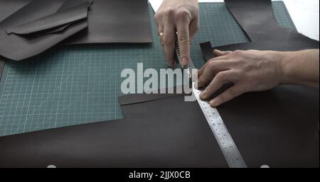 Close up of leather craftsman working with natural leather by knife and ruler by cutting a leather to a peaces. Handmade master at work in local works Stock Photo