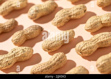 From above fresh peanuts in shells forming seamless pattern on peach background Stock Photo