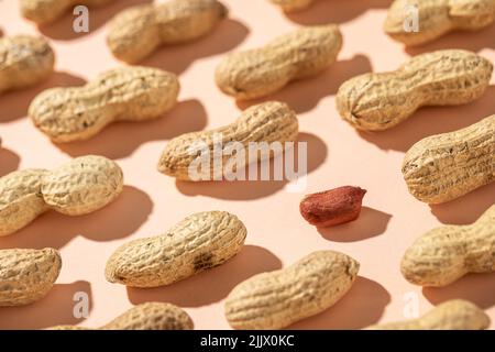 From above fresh peanuts in shells forming seamless pattern on peach background next to a peeled peanut Stock Photo