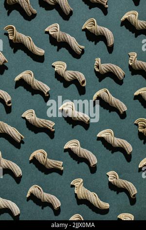 Top view of raw spiral shaped pasta arranged in order on green background Stock Photo