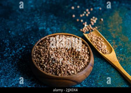 Overhead view of wooden bowl with organic and healthy raw buckwheat grain on dark concrete background Stock Photo