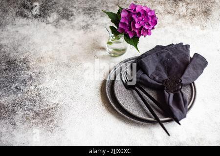 Minimalist cutlery set with purple hydrangea flowers on dark concrete table Stock Photo