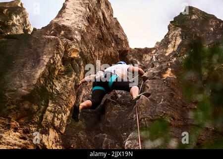 Low angle full body of active man climbing on rocky cliff Stock Photo