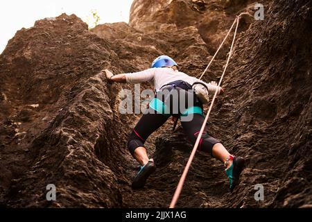 Low angle full body of active man climbing on rocky cliff Stock Photo