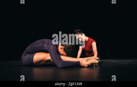 Full body male and female ballet dancers stretching on dark stage during rehearsal in theater Stock Photo