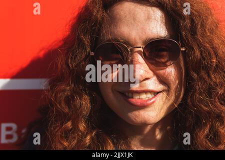 Portrait of smiling young Woman wearing sunglasses while standing against wall Stock Photo