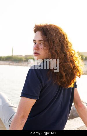 Side view of young Woman with redhead sitting against beach in city Stock Photo