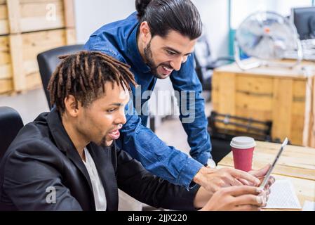 two optimistic multiracial coworkers in formal wear surfing cellphone while working with documents at table in modern light office Stock Photo