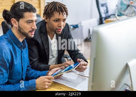 Glad diverse male employees in formal wear surfing tablet while working together on business project at table in light modern office Stock Photo