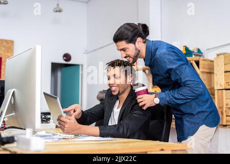 Glad diverse male employees in formal wear surfing tablet while working together on business project at table in light modern office Stock Photo