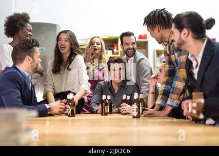 Group of smiling multiracial coworkers sitting at table with bottles of alcohol beer while spending time together in light office Stock Photo