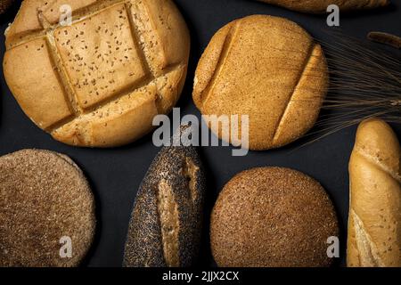 Top view mix of delicious round wholegrain bread loaves and baguettes covered with seeds placed on black background in studio Stock Photo