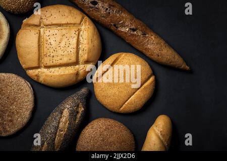 Top view mix of delicious round wholegrain bread loaves and baguettes covered with seeds placed on black background in studio Stock Photo