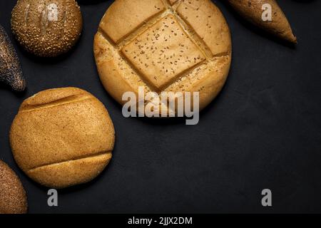 Top view mix of delicious round wholegrain bread loaves and baguettes covered with seeds placed on black background in studio Stock Photo