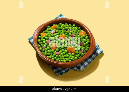 Bowl of delicious green peas with ham and carrot placed on napkin on yellow background Stock Photo