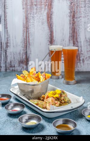Tasty fried potatoes with breaded chicken wings placed on table with set of sauces in light kitchen Stock Photo