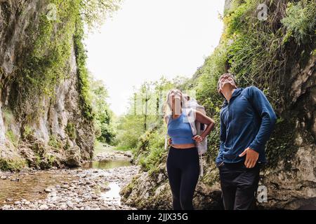 Smiling couple looking up while standing by cliff in forest Stock Photo