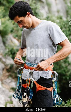 Male hiker with harness tying rope on waist while preparing form rappelling Stock Photo