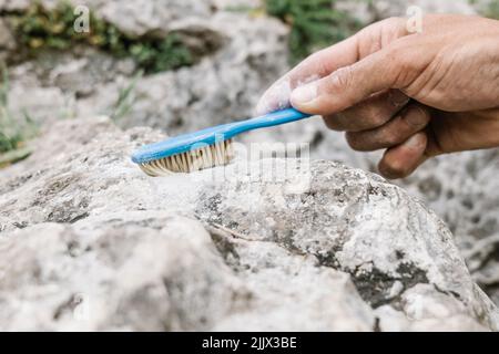 Closeup of cropped hand cleaning rock with toothbrush Stock Photo