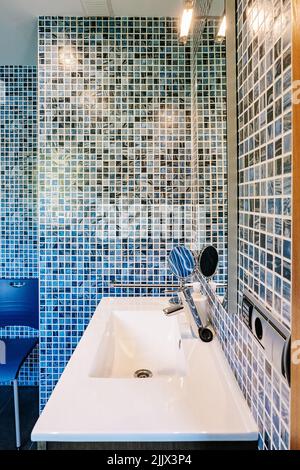 White ceramic sink with chrome faucet and cosmetic mirror in contemporary bathroom with blue mosaic tiled walls Stock Photo