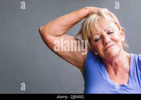 Fit senior Woman doing neck exercise sitting with eyes closed on yoga mat Stock Photo