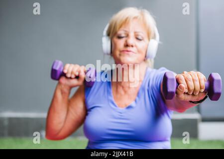 Fit senior Woman exercising with purple dumbbells representing active lifestyle with eyes closed Stock Photo