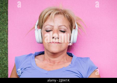 Top view closeup of senior Woman listening music with closed eyes lying on yoga mat Stock Photo