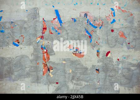 Colorful stains under crumbling gray paint on shabby wall of grungy building on street Stock Photo