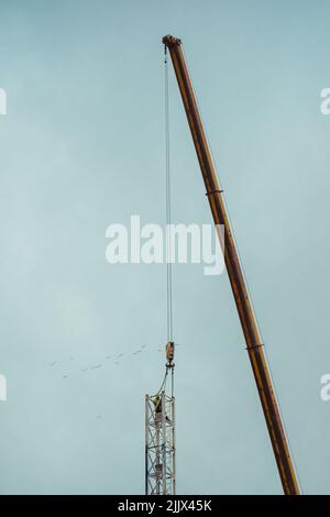 Low angle of tall crane lifting and installing metal structure against overcast gray sky on construction site Stock Photo