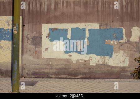 Weathered concrete wall with graffiti covered with crumbling gray paint on city street in daytime Stock Photo