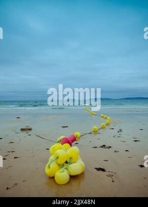 Bunch of bright yellow buoys on rope located on wet sandy beach near waving sea on stormy day in Rias Baixas, Spain Stock Photo