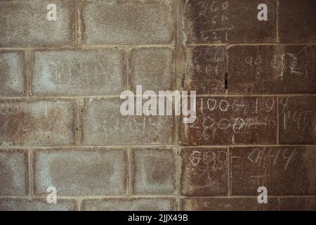 Weathered brick wall of grungy building with scratched digits and equations on street Stock Photo