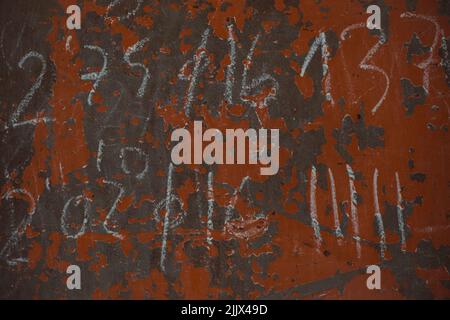 Rows of numbers written with chalk on weathered red and black painted wall Stock Photo