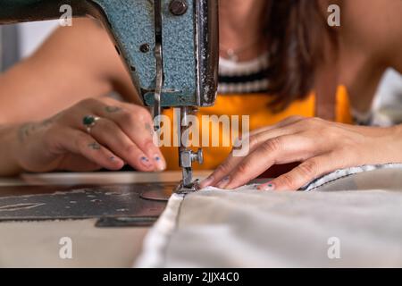 Anonymous adult female artisan in apron sewing fabric with machine while working in traditional workshop Stock Photo