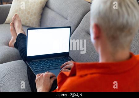 Transgender man using laptop sitting on sofa in living room Stock Photo