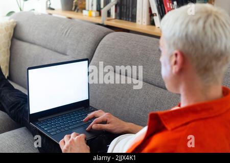 Transgender man using laptop sitting on sofa in living room Stock Photo