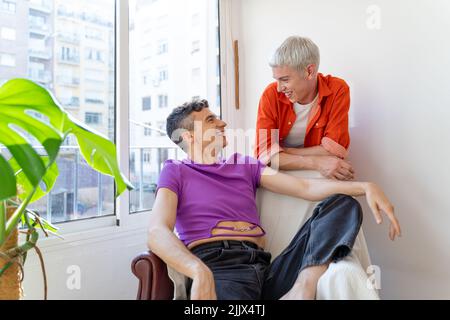 Cheerful gay man talking while looking at boyfriend near window at home Stock Photo