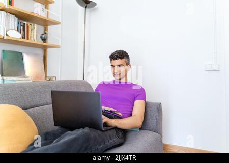 Transgender man using laptop sitting on sofa in living room Stock Photo