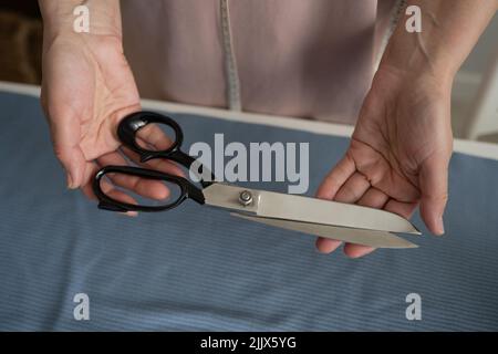 From above of crop anonymous dressmaker with metal scissors standing near table with fabric while working in professional light workshop Stock Photo